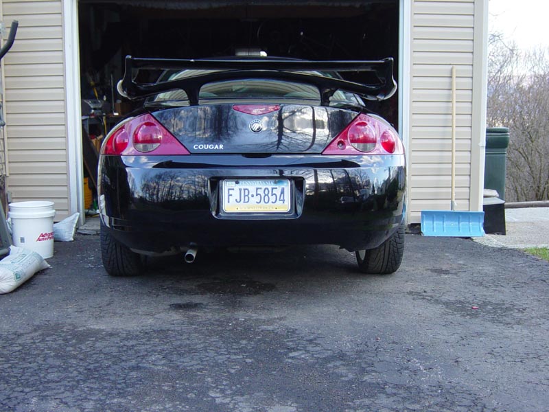 Rear of black Mercury Cougar coupe with spoiler parked at garage