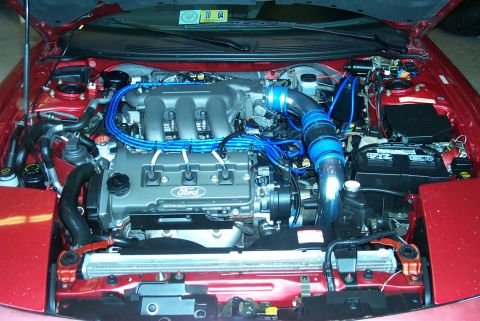 1996 Ford Probe - Engine bay of a 1996 Ford Probe, a V6 engine with custom blue wiring and intake piping.