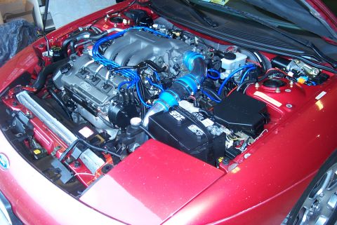 1996 Ford Probe - The engine bay of a red car features a V6 engine with prominent blue wiring and a black battery.