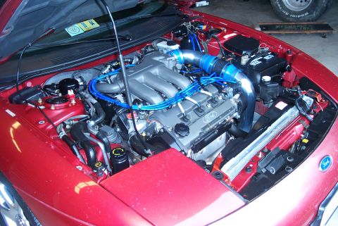 1996 Ford Probe - The engine bay of a red 1996 Ford Probe, showing the V6 engine with custom blue wiring and chrome intake.