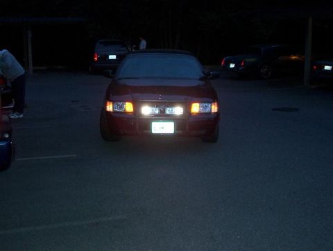 2001 Ford Crown Victoria - A red sedan is parked at night, with its headlights illuminating the area. Other vehicles are visible in the background.