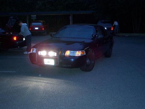2001 Ford Crown Victoria - A dark sedan with a push bar is parked at night, with its headlights illuminated.