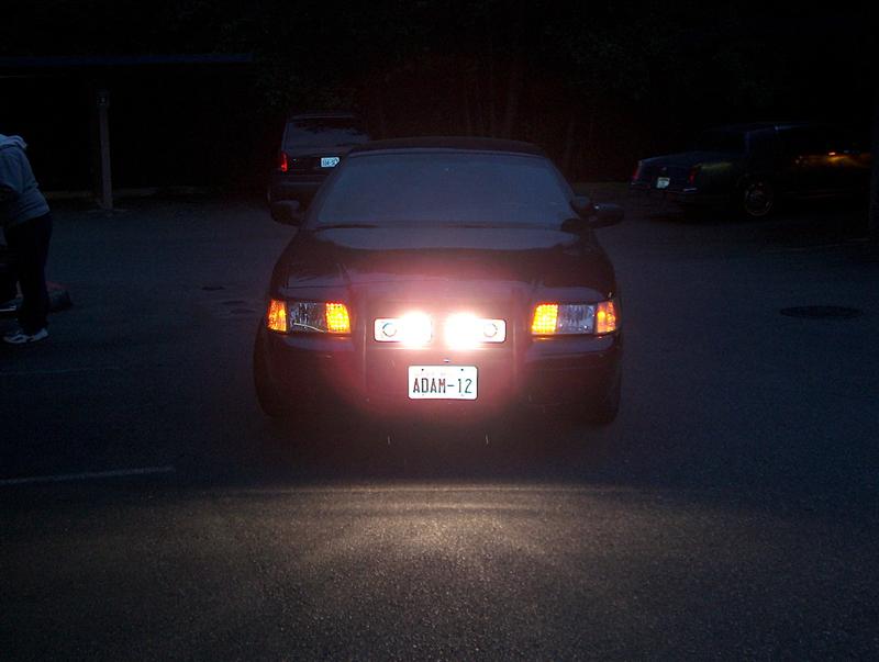 2001 Ford Crown Victoria front view, auxiliary lights on, license plate ADAN-12. Another vehicle visible in background