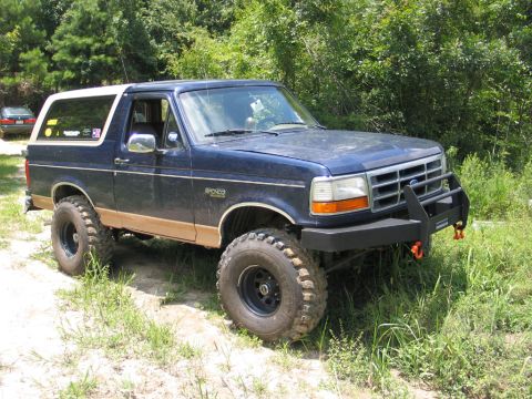 1995 Ford Bronco - This 1995 Ford Bronco features off-road tires and a custom brush guard, parked outdoors.