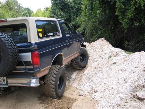 1995 Ford Bronco - 1995 Ford Bronco navigates a challenging off-road terrain with large tires.