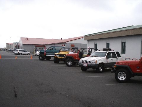 1996 Ford Bronco - A row of off-road vehicles, including Jeeps and a lifted truck, are parked in a lot on a cloudy day.