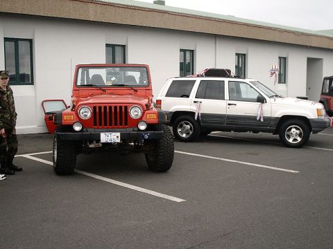 1996 Ford Bronco - A red Jeep Wrangler is parked in front of a building, with a white SUV also visible in the background.