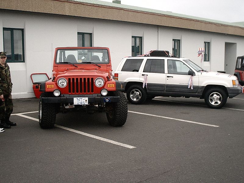 Red lifted Jeep Wrangler and white Jeep Grand Cherokee parked in a lot