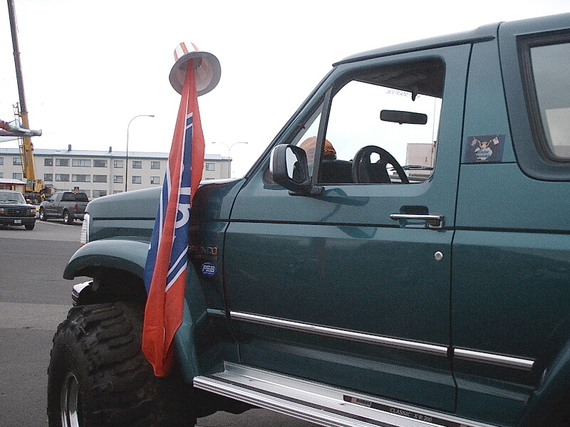 Dark green lifted Ford Bronco with big tires and a flag on the side mirror