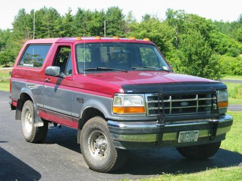1995 Ford Bronco - Front three-quarter view of a red-over-silver two-tone full-size Ford Bronco with a black brush guard over the chrome grille, smoked hood d…
