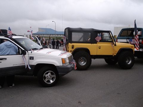 1996 Ford Bronco - Two vehicles, a white Jeep Grand Cherokee and a yellow off-road vehicle, are parked together, adorned with patriotic decorations.