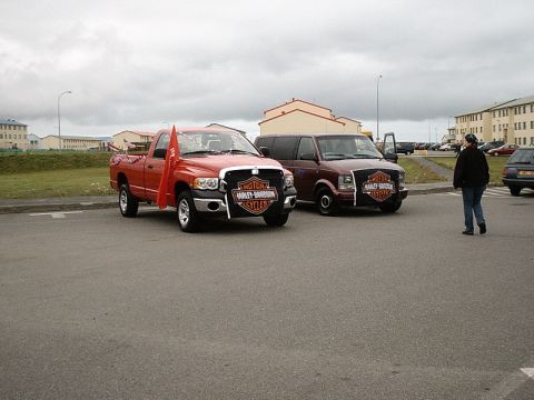 1996 Ford Bronco - Two vehicles, a red pickup truck and a maroon van, are parked side-by-side, both displaying Harley-Davidson banners.