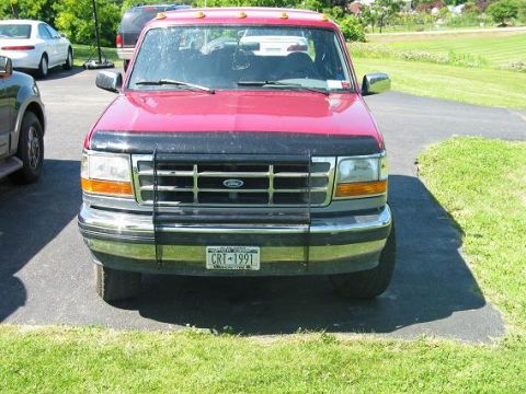 1995 Ford Bronco - Head-on front view of a red 1990s Ford truck parked on a paved driveway beside a green lawn, fitted with a black tubular brush guard over t…