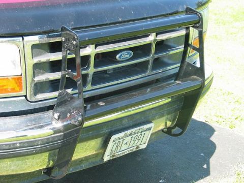 1995 Ford Bronco - Close-up front view of a dark green/black Ford truck showing the chrome grille with blue Ford oval emblem, amber turn signals, and a black…