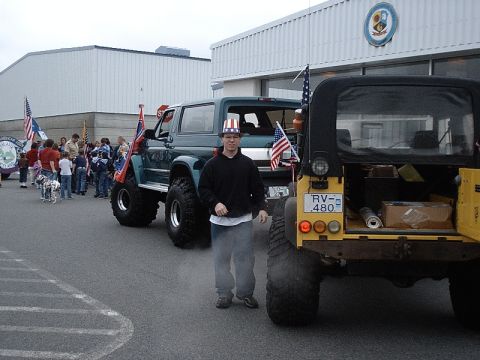 1996 Ford Bronco - A lifted 1996 Ford Bronco, decorated with American flags, participates in a parade alongside other vehicles.