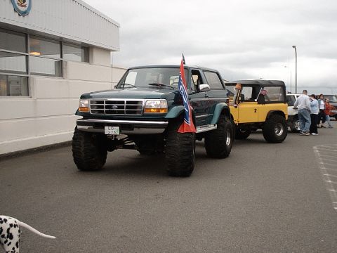 1996 Ford Bronco - A modified green Ford Bronco is parked next to a yellow Jeep, with people standing nearby.