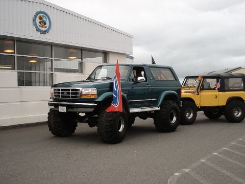 1996 Ford Bronco - A lifted green 1996 Ford Bronco is parked next to a yellow off-road vehicle, both displaying American flags.