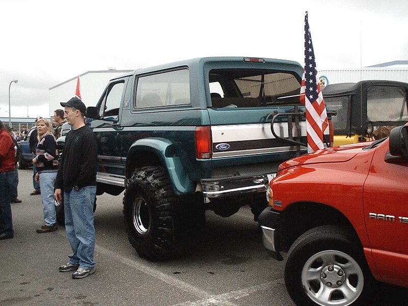 Lifted teal Ford Bronco rear view with US flag beside red Dodge Ram at car show