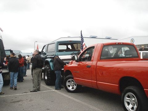 1996 Ford Bronco - A teal Ford Bronco is parked next to a red pickup truck with people milling around.