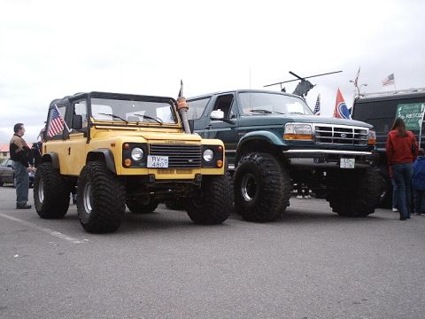 1996 Ford Bronco - Two modified off-road vehicles, a yellow Land Rover and a green Ford truck, are parked together.