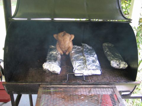 1995 Ford Bronco - A whole chicken is being smoked alongside foil-wrapped items on a large barbecue grill.