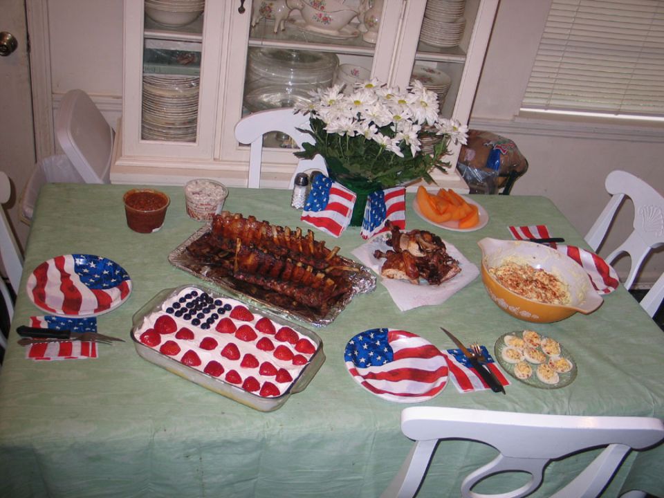 Table set with a patriotic theme, ribs, chicken, fruit, deviled eggs, and a strawberry-blueberry dessert