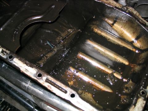 1986 Ford F-150 - A heavily soiled oil pan with visible sludge and grime, indicating potential engine issues.