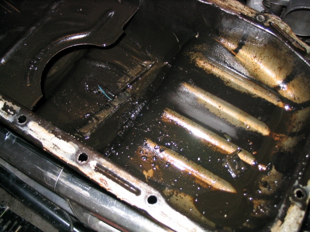 Dirty oil pan with sludge and debris, showing internal ribs and bolt holes