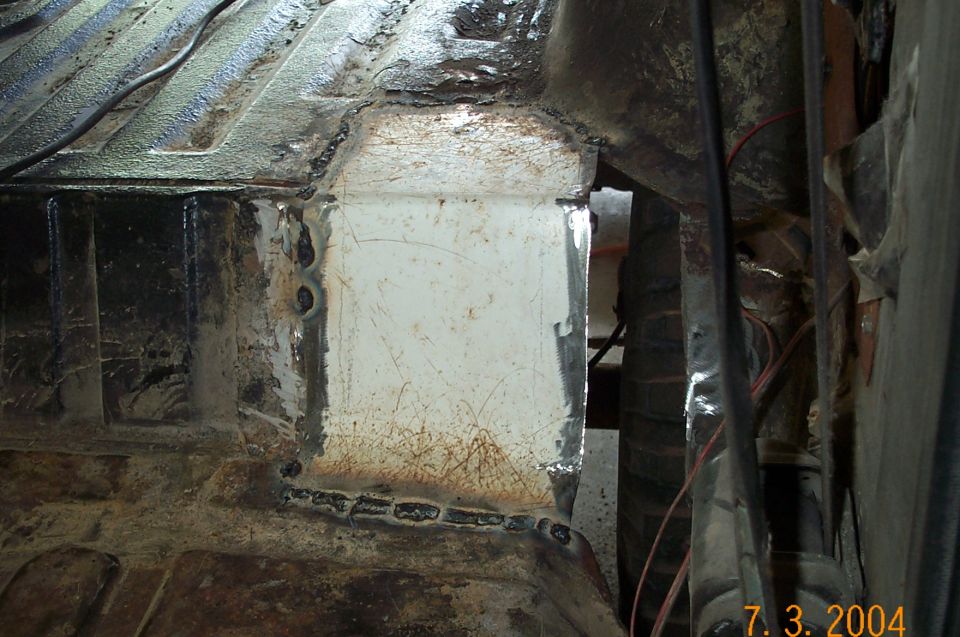 Fresh weld repair on rusty undercarriage frame section, new white patch panel welded into floor