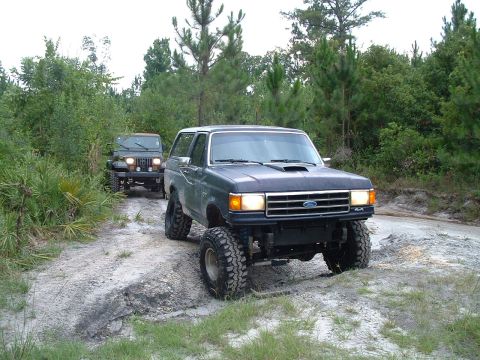 1995 Ford Bronco - Two off-road vehicles, a Ford Bronco and a Jeep Wrangler, navigate a sandy trail.