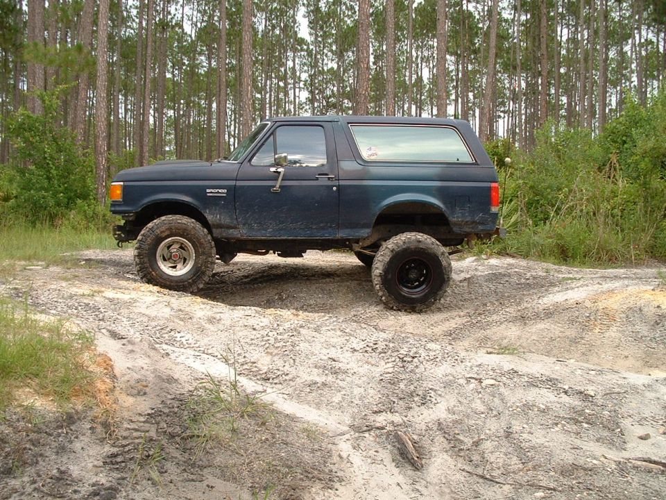 Dark blue Ford Bronco on dirt track, lifted with large tires
