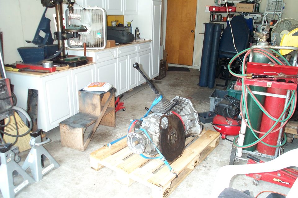 Transmission with shifter strapped to a wooden pallet in a garage workshop