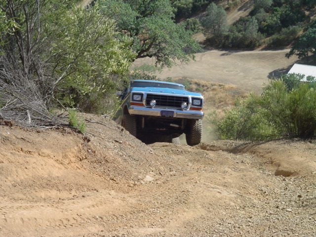 Blue 1978 Ford Bronco driving off-road on a dirt hill