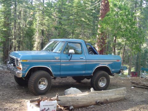 1978 Ford Bronco - A blue 1978 Ford Bronco sits parked on a dirt path surrounded by trees.