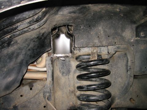 1985 Ford Bronco - This image shows a close-up view of a vehicle's suspension system, focusing on the coil spring and its mounting bracket.