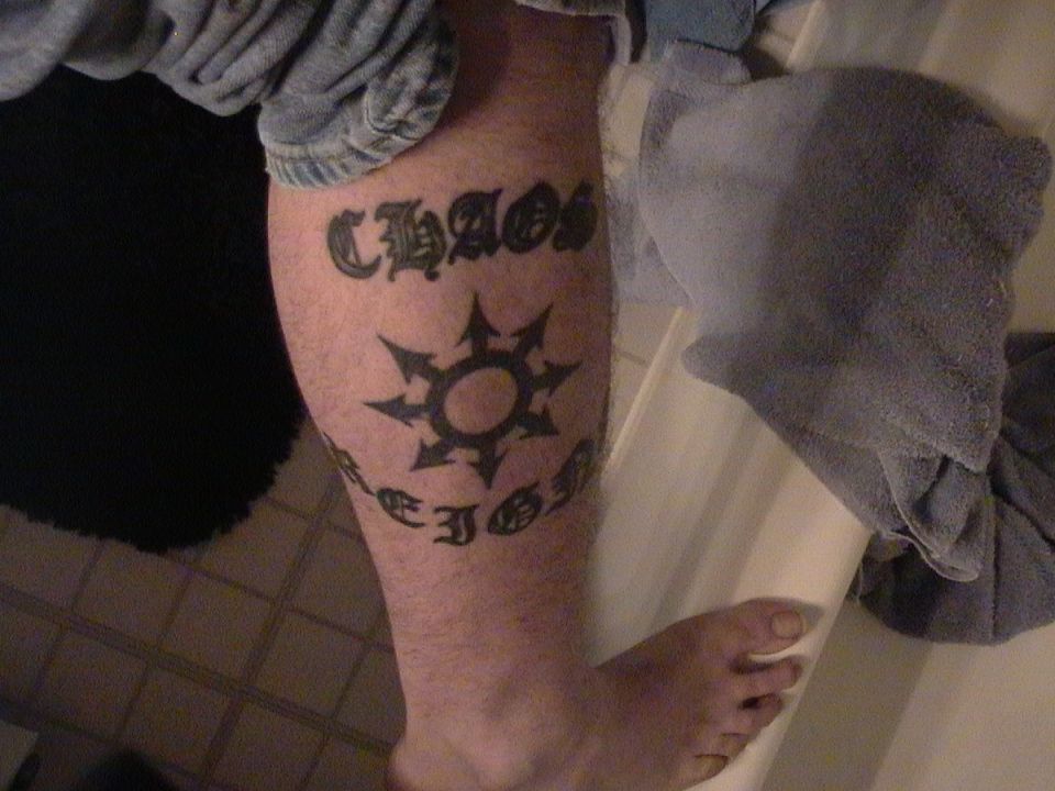 Black ink calf tattoo reading CHAOS REIGNS around an eight-point chaos star