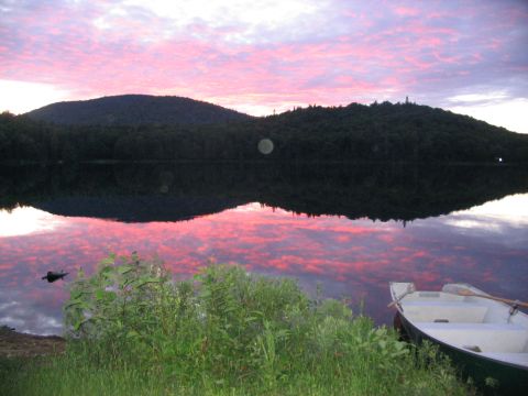 1986 Ford Bronco - A lake reflects the vibrant pink and purple hues of a sunset sky, with tree-covered mountains in the background.