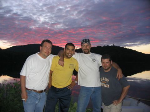 1986 Ford Bronco - Four men pose for a photo by a lake during a vibrant sunset, with a wooded hill in the background.