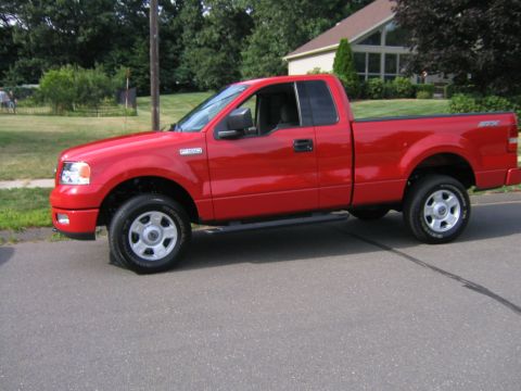 1994 Ford Bronco - A red pickup truck is parked on the side of a residential street on a sunny day.
