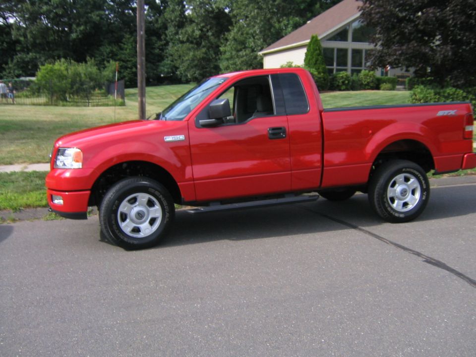 Red Ford F-150 STX regular cab pickup, driver-side profile view on a residential street