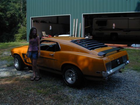 1988 Ford Bronco - A classic orange Mustang is parked outside a garage with a woman posing beside it.