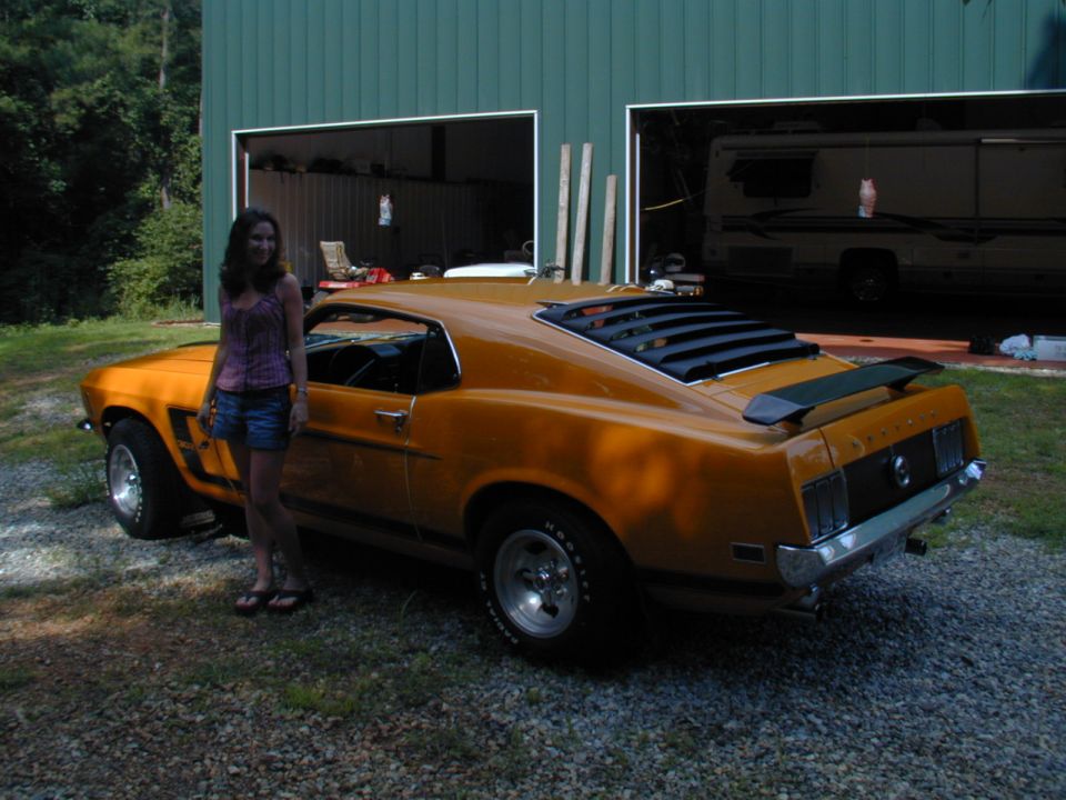 Orange 1969 Ford Mustang Boss 302 parked in front of a garage with a woman standing next to it
