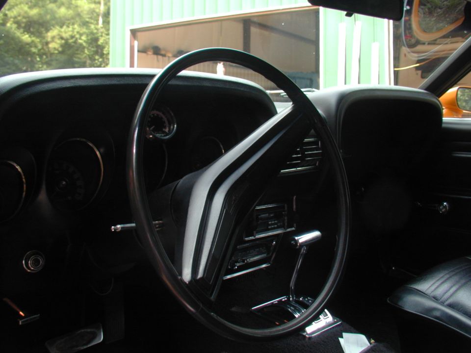 Car interior with black steering wheel, dashboard, and seats. Chrome shifter visible