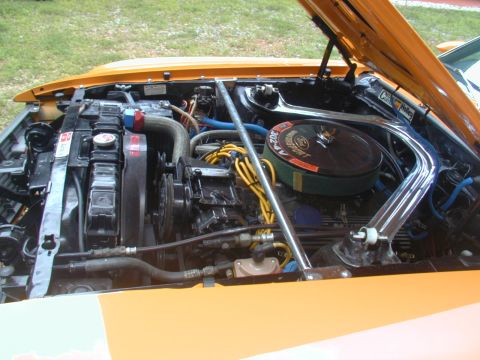1988 Ford Bronco - The engine bay of an orange vehicle is visible, a V8 engine with yellow spark plug wires and a chrome strut tower brace.
