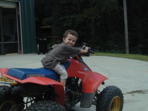 1988 Ford Bronco - A young boy smiles while sitting on a red ATV with a blue seat.