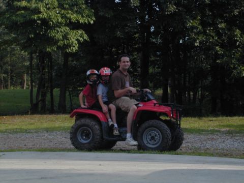 1988 Ford Bronco - A man and two children ride on a red ATV through a grassy area with trees in the background.