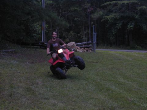 1988 Ford Bronco - A man rides a red ATV on its back wheels in a grassy outdoor setting.