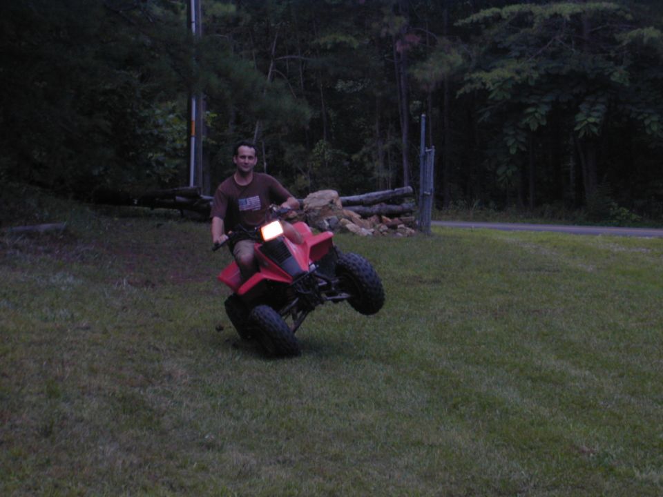Red ATV with a man riding it on its rear wheels in a grassy area