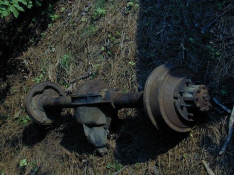 1988 Ford Bronco - A rusty rear axle assembly lies on the ground, showing its differential and drum brakes.