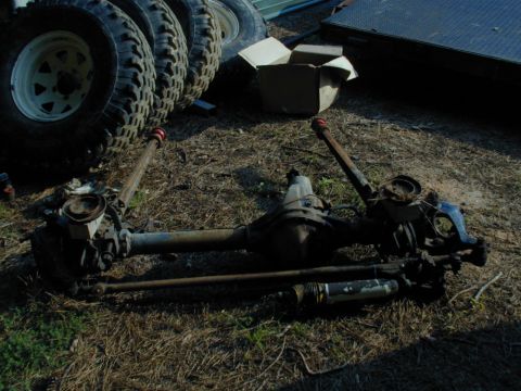 1988 Ford Bronco - Front and rear axles are laid out on the ground with a stack of tires visible behind them.